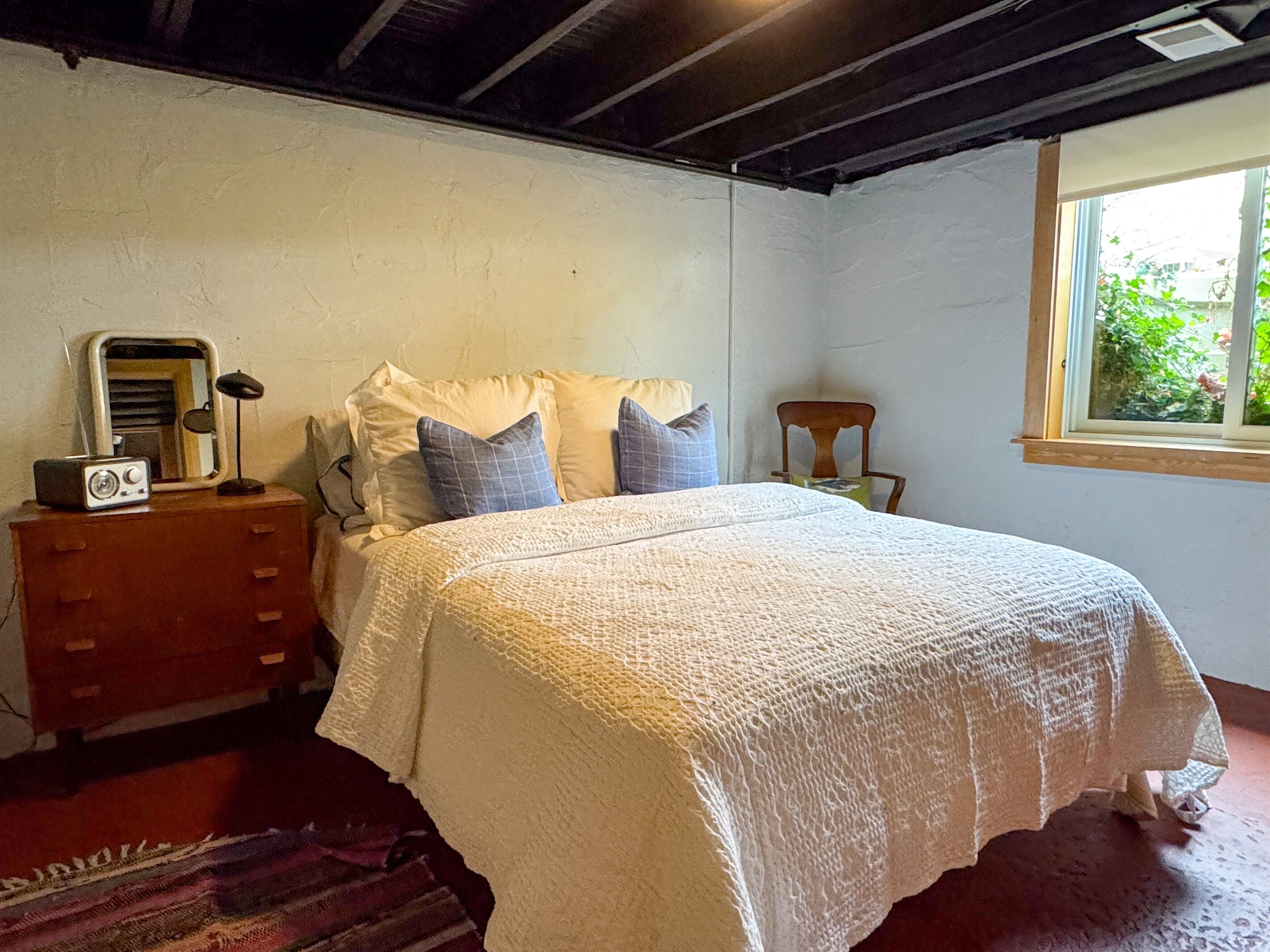 Une chambre à coucher avec un lit, une commode, une chaise et une fenêtre.
