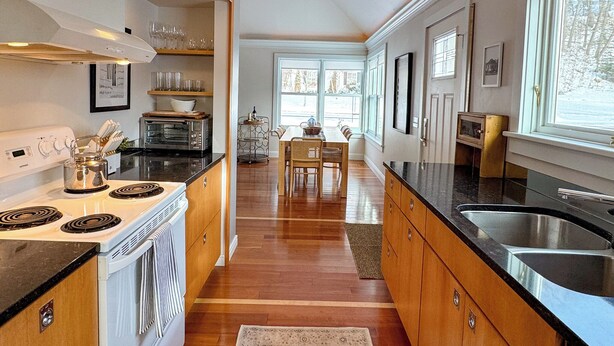 A modern kitchen with a central island, built-in oven, and a dining area with a view of the outdoors. - The Ingalls House - Downtown (Harbor Springs)
