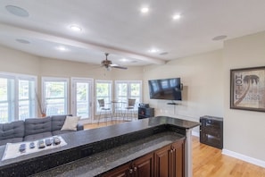 A modern kitchen with a granite countertop, a ceiling fan, and a flat-screen TV mounted on the wall. - Sun Realty gorgeous oceanside retreat with an elevator in Corolla NC! (Corolla)