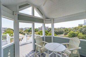 A covered outdoor deck with a table and two chairs, overlooking a residential area with houses and greenery.