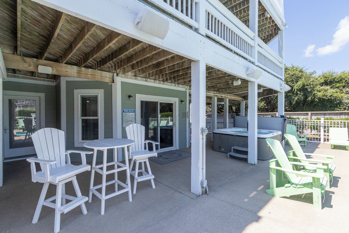 Un espace extérieur abrité avec des chaises Adirondack et une table, une piscine avec un panneau indicateur et un jacuzzi.