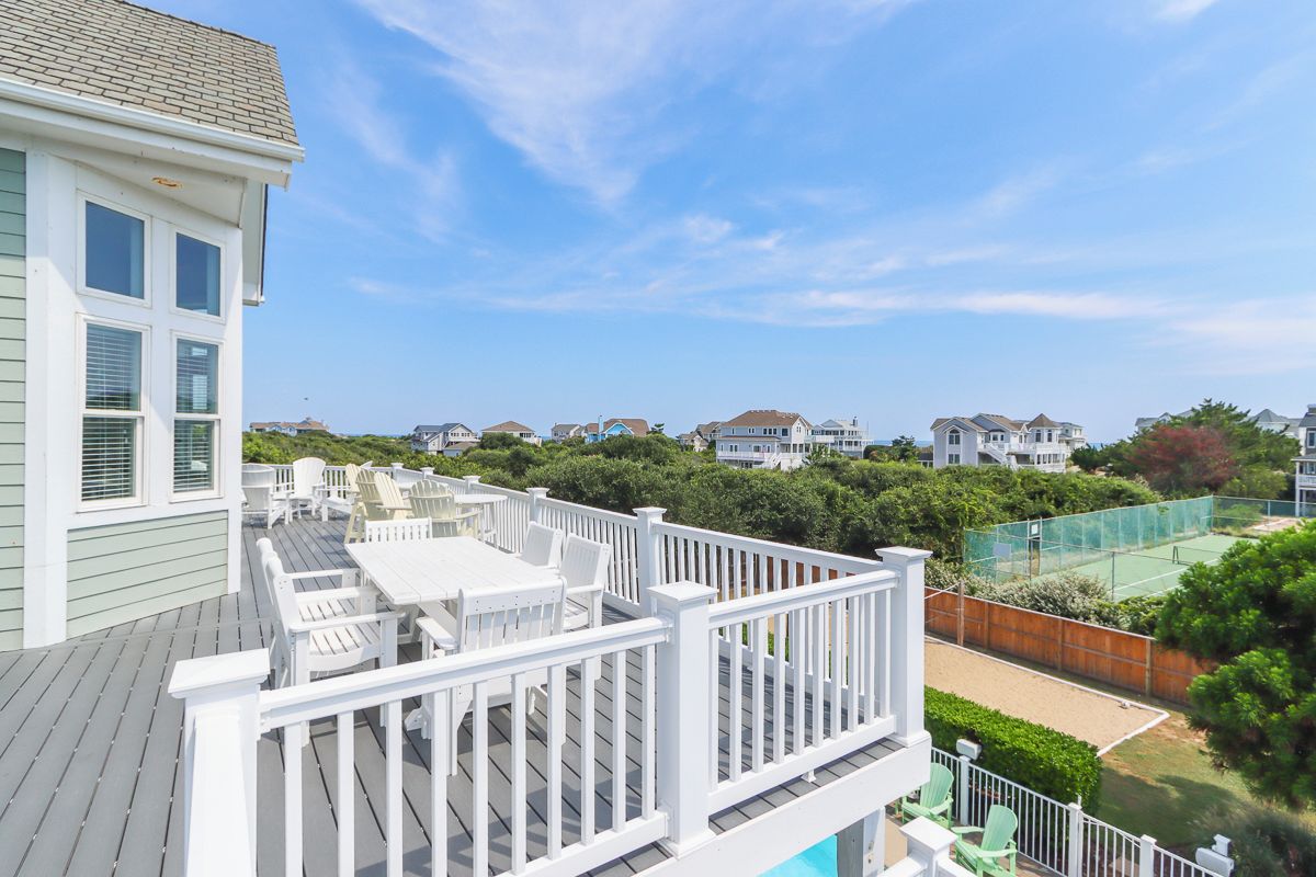 Une terrasse aménagée avec du mobilier d’extérieur, un court de tennis et une vue sur les maisons voisines.