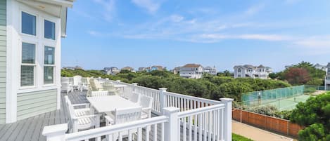 A residential deck with outdoor furniture, a tennis court, and a view of neighboring houses.