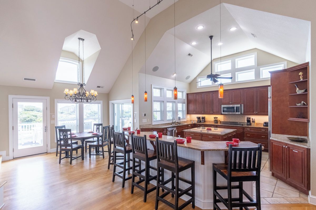 A spacious kitchen with a high ceiling, large windows, and a central island with bar stools.