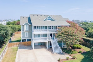 A two-story house with a front porch, a covered front deck, and a staircase leading to the deck. - Sun Realty gorgeous oceanside retreat with an elevator in Corolla NC! (Corolla)