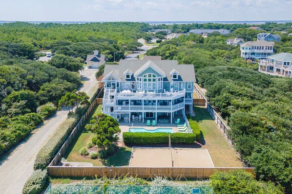 A large, multi-story house with a prominent front porch and a swimming pool.
