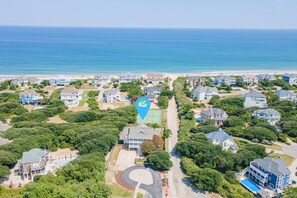 An aerial view of a coastal residential area with houses, a tennis court, and a beach.
