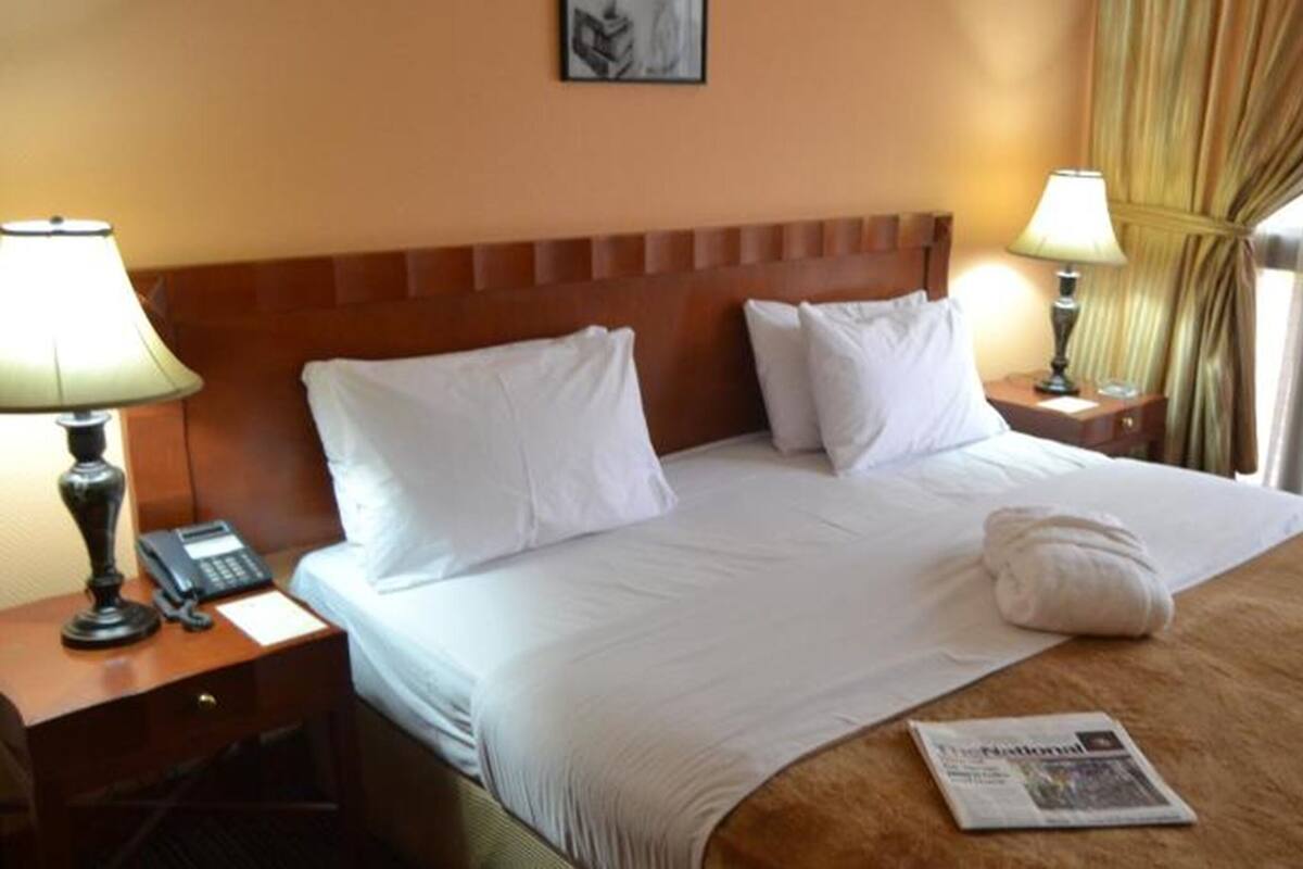 Een hotelkamer met een groot bed, twee nachtkastjes met lampen, een telefoon en een krant op het bed.