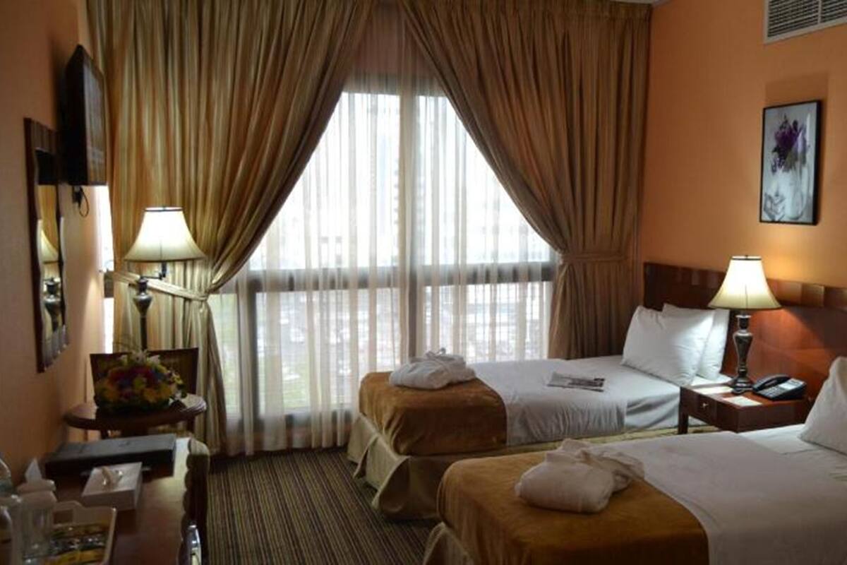Een hotelkamer met twee bedden, een bureau, een stoel, een lamp en een raam met gordijnen.