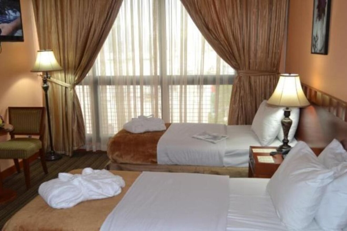 A hotel room with two beds, a sitting area with a chair, a lamp, and a window with curtains.