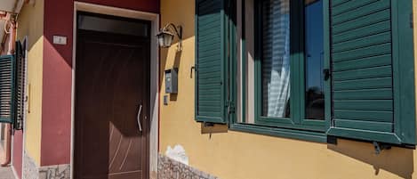 Un edificio con base de piedra, puerta de madera y contraventanas verdes.