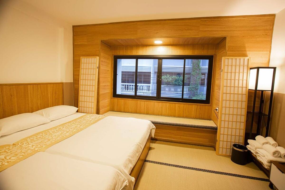 A hotel room with two beds, a window with a view, a wooden headboard, and a bedside table with towels.