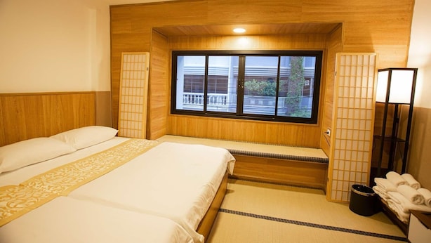 A hotel room with two beds, a window with a view, a wooden headboard, and a bedside table with towels. - Dado9 (Bangkok)