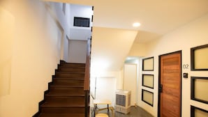 A staircase leading to an upper floor, a small table with a chair, an air conditioning unit, and a wooden door with the number 02. - Dado9 (Bangkok)
