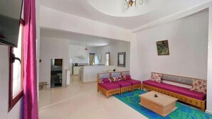 A living room with a sofa set, a coffee table, and a kitchen area in the background. - Sweet Villa Residence (Houmt Souk)