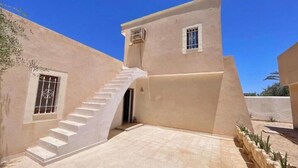A building with a beige exterior, a staircase leading to a door, and a small window with bars. - Sweet Villa Residence (Houmt Souk)