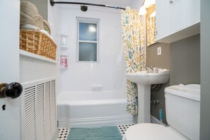 A small bathroom with a bathtub, a window, a sink, and a toilet.