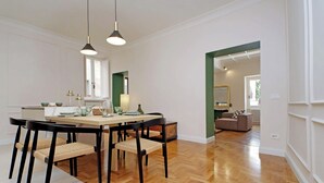 Un comedor con una mesa y sillas de madera, una cocina al fondo y una sala de estar con un sofá y un espejo.