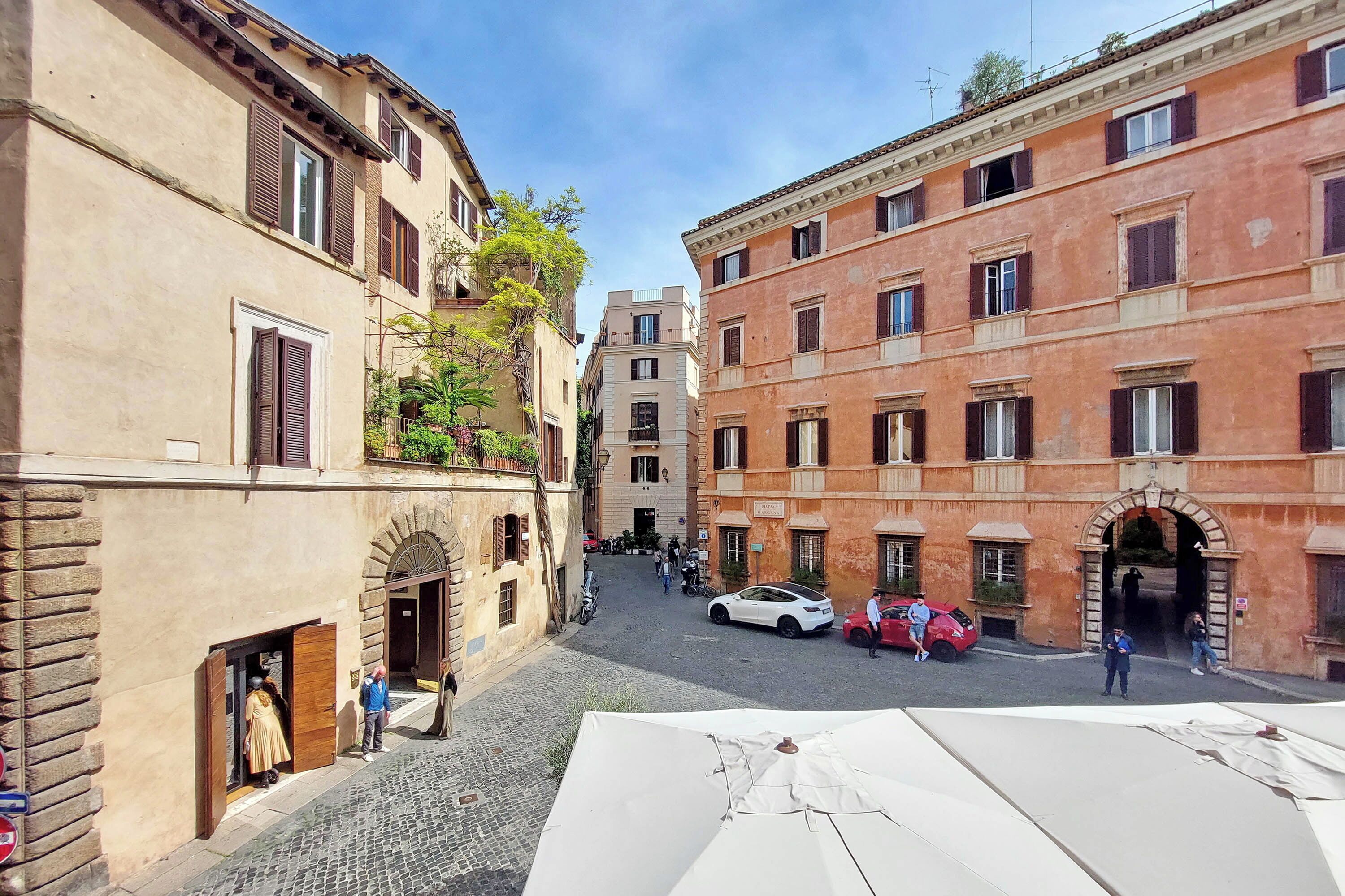 A narrow street with buildings on either side, a cobblestone road, and a few parked cars.