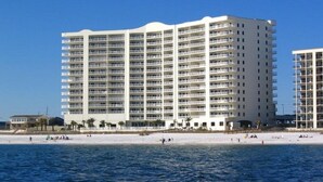A large, multi-story hotel with balconies, located near a beach with people in the water. - Admirals Quarter 908, 3 bedroom, 3 bath coastal oasis (Orange Beach)