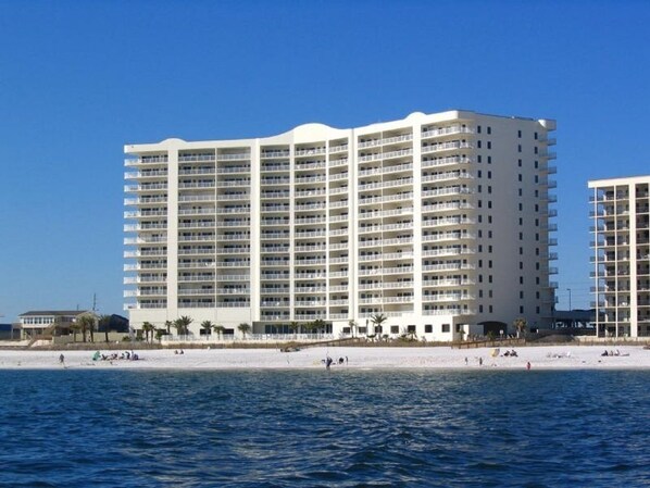 A large, multi-story hotel with balconies, located near a beach with people in the water. - Admirals Quarter 908, 3 bedroom, 3 bath coastal oasis (Orange Beach)
