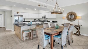 A modern kitchen with white cabinets, a stainless steel refrigerator, and a central island with bar stools. - Admirals Quarter 908, 3 bedroom, 3 bath coastal oasis (Orange Beach)