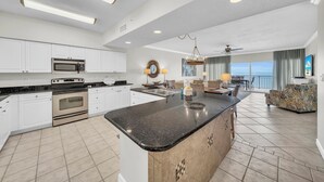 A spacious kitchen with white cabinets, a large island, and a dining area with a view. - Admirals Quarter 908, 3 bedroom, 3 bath coastal oasis (Orange Beach)