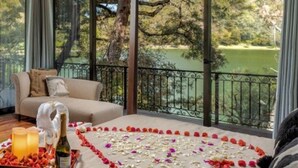 Ein gemütlicher Balkon mit einer herzförmigen Anordnung aus Rosenblättern und einer Champagnerflasche auf einem Tablett, mit Blick auf eine üppige grüne Landschaft.