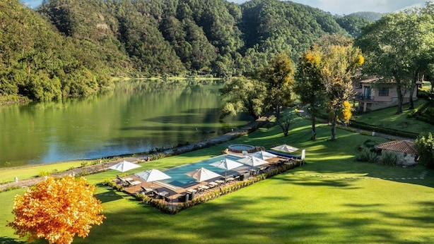 Ein Resort mit Schwimmbad, Liegestühlen und Blick auf einen See und bewaldete Hügel.