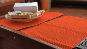 Une table en bois sur laquelle se trouvent une assiette de sandwichs, une boîte blanche, un gobelet en métal et un tapis orange.