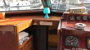 Un poste de commande de bateau, avec un bureau en bois, une lampe bleue et divers indicateurs et cadrans.