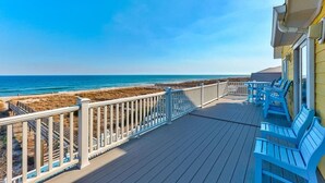 A wooden deck with blue chairs and a white railing overlooking a beach. - Big Bird -7br-Oceanfront-Heated Pool-Elevator (Kure Beach)
