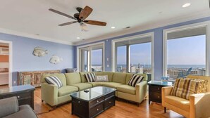 A living room with a sectional sofa, a coffee table, and a ceiling fan. - Big Bird -7br-Oceanfront-Heated Pool-Elevator (Kure Beach)