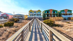 A wooden boardwalk leading to colorful beach houses with a clear sky. - Big Bird -7br-Oceanfront-Heated Pool-Elevator (Kure Beach)