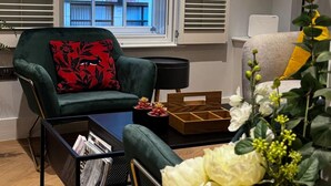 A modern living room with a green armchair, a black coffee table with magazines, a wooden side table, and a large window with blinds. - London Charm - Central London Apart Soho Mayfair (London)