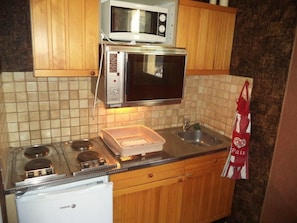 A kitchen with a stove, microwave, and oven. There is a sink and a cabinet above the stove.