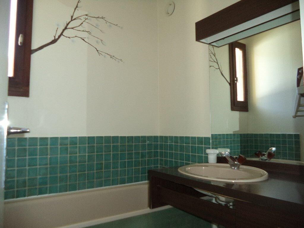 A bathroom with a sink, mirror, and green-tiled walls.