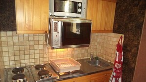Una cocina con estufa, microondas y horno. Hay un lavamanos y un armario sobre la estufa.