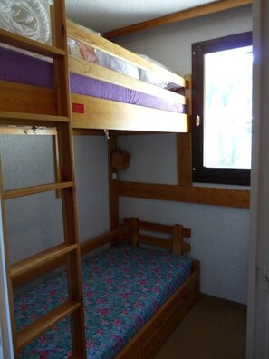 Une chambre avec un lit superposé, une fenêtre, une étagère et un petit panier suspendu.