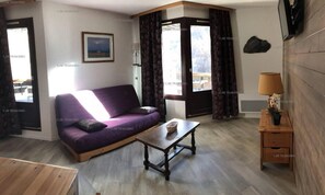A living room with a purple sofa, a wooden coffee table, and a small wooden side table with a lamp.