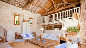 Een rustiek interieur met stenen muren, houten balken, rieten meubels en een balkon met opengeschoven hoeden.