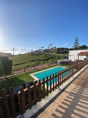 Una piscina con una valla de madera, cielo despejado y un paisaje montañoso al fondo.