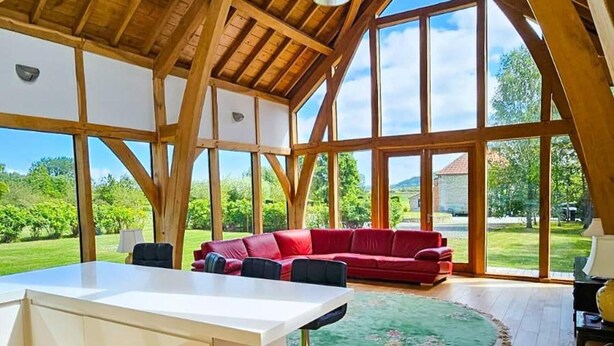 Ein geräumiger Raum mit hoher Decke und großen Fenstern, einem roten Sofa und einem Esstisch.