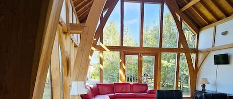 Ein geräumiger Raum mit hoher Decke und großen Fenstern, ein rotes Ledersofa und ein weißer Tisch.
