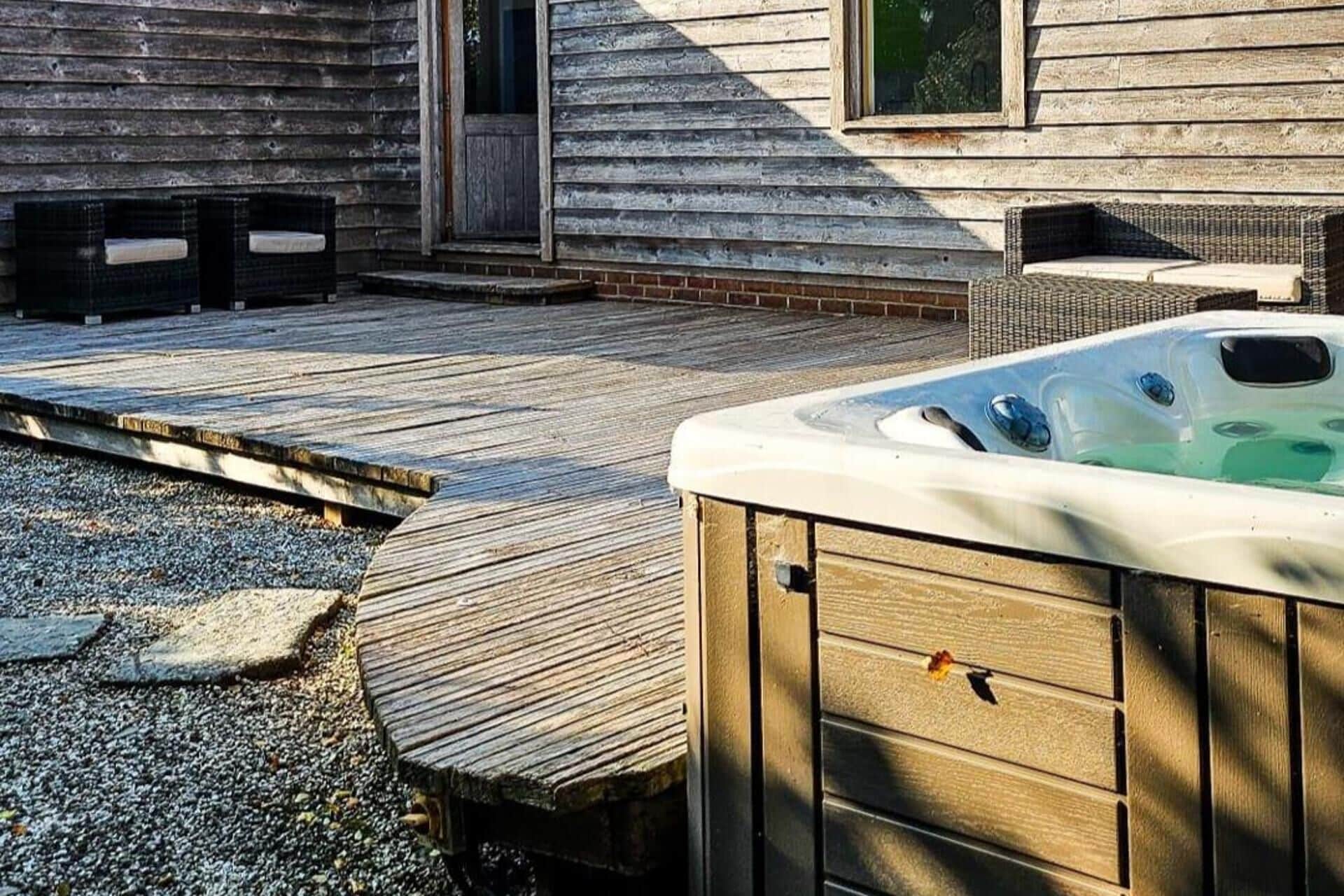Une terrasse en bois avec un jacuzzi, un patio en briques et un petit espace salon extérieur.