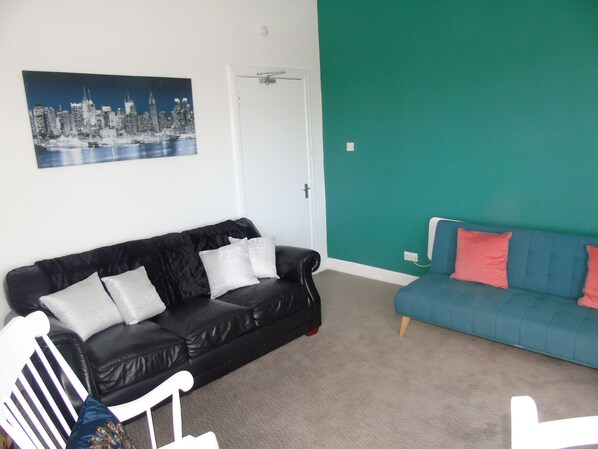 A living room with a black leather sofa, a blue sofa, and a white chair. There is a door and a wall with a teal color.
