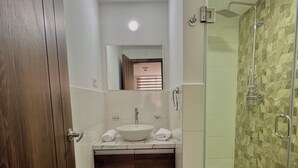 A bathroom with a marble floor, a white sink, a glass shower enclosure, and a wooden door. - Hotel RYA Center (Ibarra)