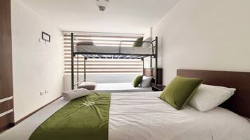 Dormitorio con literas, una manta verde, ropa de cama blanca y un cabecero de madera.