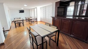 A spacious living area with a dining table and chairs, wooden flooring, a kitchen with dark cabinets, and a large window with blinds. - Hotel RYA Center (Ibarra)