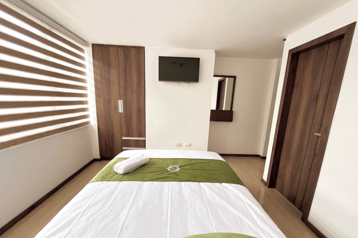 A hotel room with a bed, a television, a wardrobe, and a mirror.